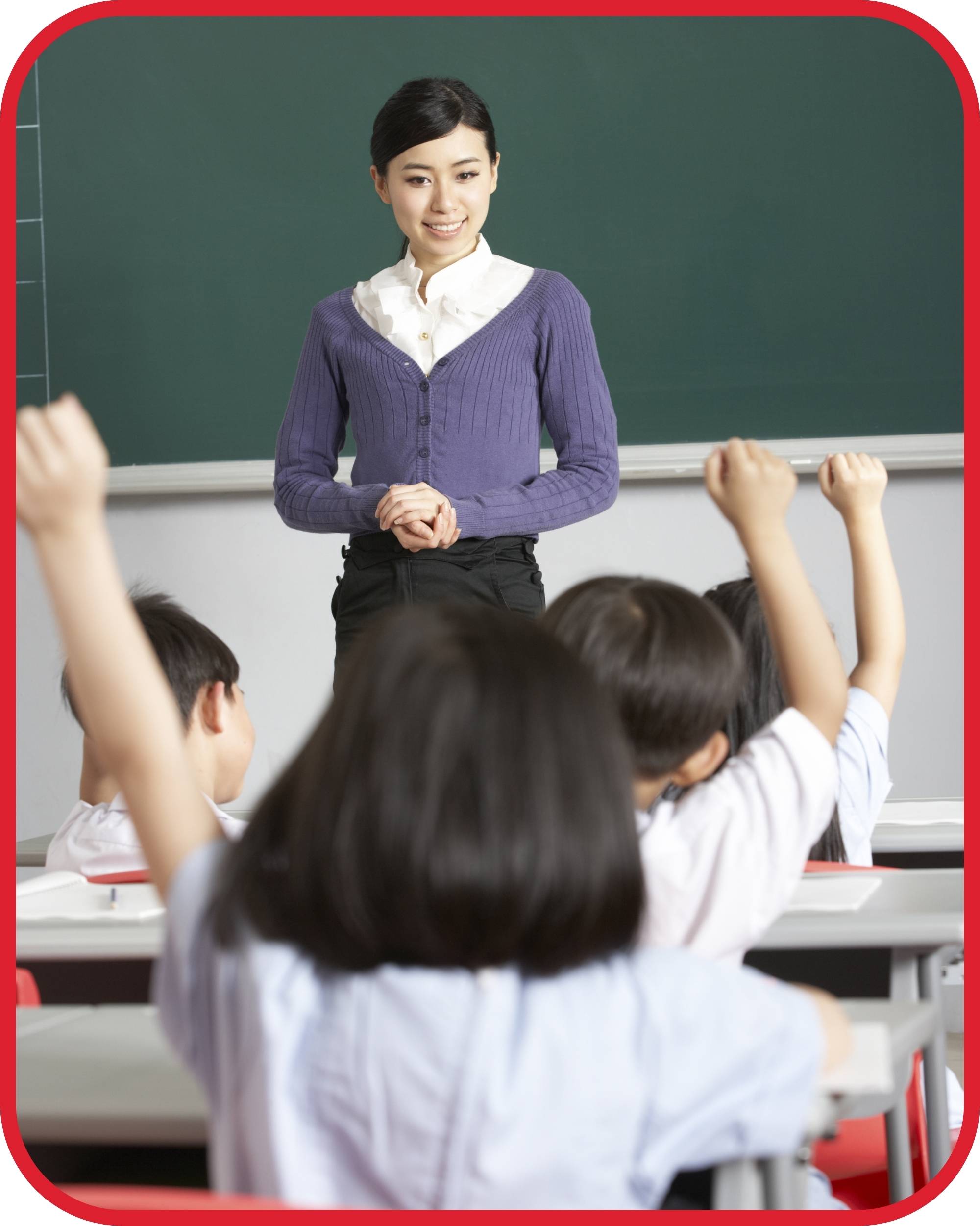 Joven profesora china en una clase de niños sentados en pupitres con pizarra negra detrás